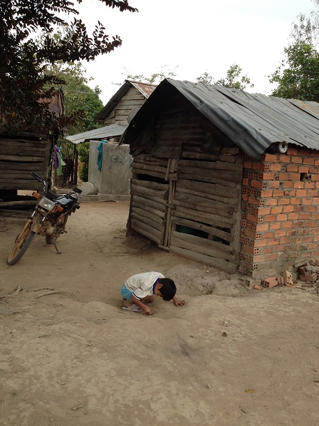 Ảnh em Số chơi một mình trong sân đất bột bên hông nhà.