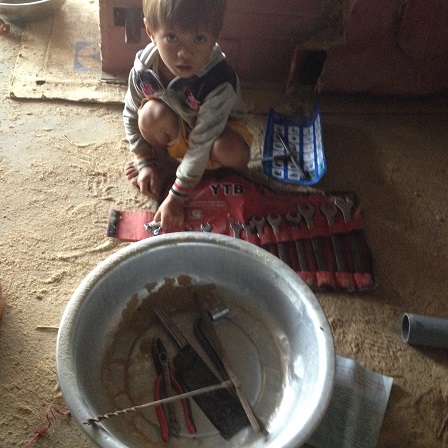 Em Anh con bố mẹ Thân ngồi chơi dưới đất bột với những dụng cụ sửa máy của bố.