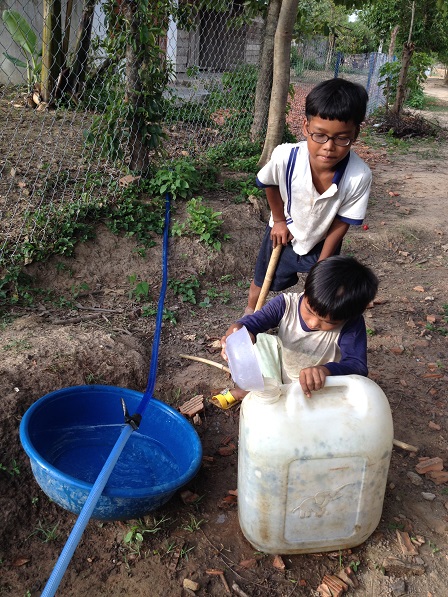 Em Xây và em Số tận dụng múc từng giọt nước chảy từ ống dây bị thủng đem về dùng.