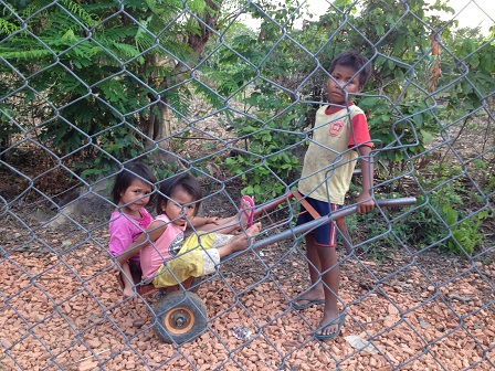 Ảnh ba em nhỏ chơi xe trước hàng rào nhà Yăh