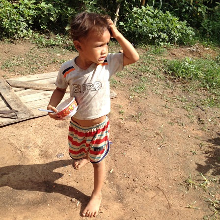 Em Khel vừa ăn cơm vừa đi ra vườn chơi.