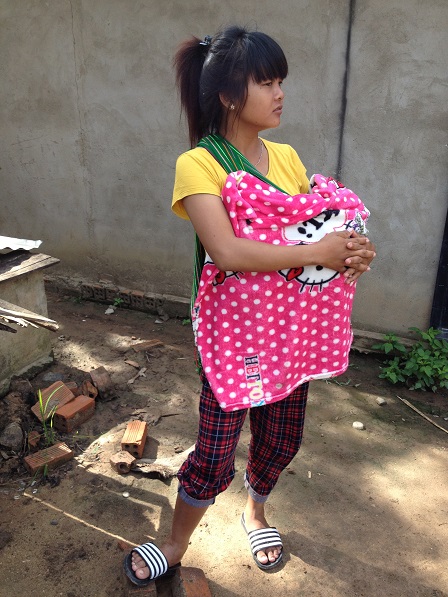 Em Huôm mười chín tuổi địu đứa con một tháng tuổi chơi trước nhà _ Buôn Hằng